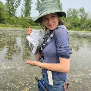 Sophia Holmes in a pond holding up a specimen bag